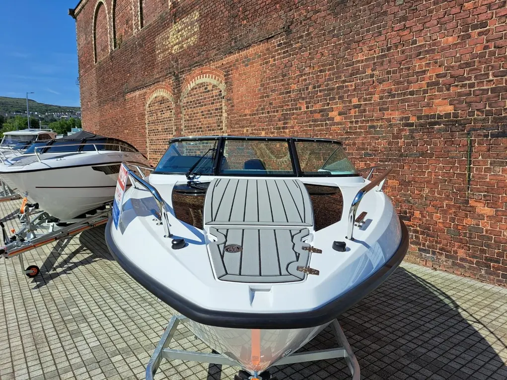 A white motorboat on display near a brick wall, showcasing its sleek design and deck layout under clear blue skies.